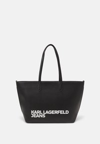 Črna torba iz teksturiranega materiala z dvema ročajema. Na sprednji strani je bel napisan logotip: "KARL LAGERFELD JEANS".