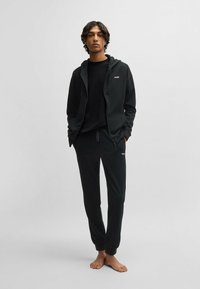 Svart hoodie och sweatpants-set. Hoodien har en framzipper och en logo. Mjuk textur, avslappnad passform och jogger-style manschetter på byxorna.