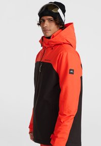 Heren snowboardjas met een feloranje bovenstuk en zwarte onderstukken, voorzien van een rits aan de voorkant, een capuchon en een logo op de mouw.