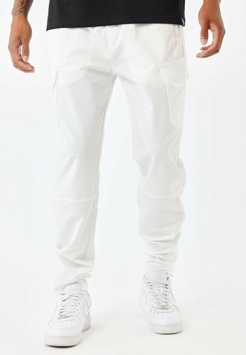 Pantalones cargo blancos hechos de una tela suave, con bolsillos laterales y un ajuste entallado. Combinados con zapatillas blancas para un look completo.