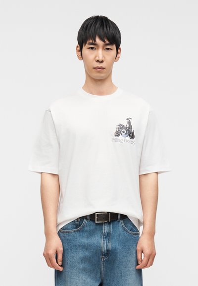 Λευκό βαμβακερό T-shirt με κοντά μανίκια, με γραφικό τύπωμα στο στήθος. Συνδυάζεται με μπλε τζιν παντελόνι και μαύρη ζώνη.