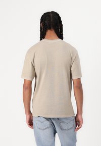 Lys beige T-shirt med korte ærmer og rund halsudskæring, der har synlige sømdetaljer, sammen med lyseblå jeans med design af dobbelt baglomme.