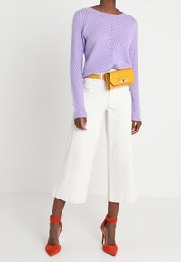 Pull tricot lilas, pantalon blanc à jambes larges, sac bandoulière jaune et chaussures à talons rouges. Pull texturé avec motif diagonal.