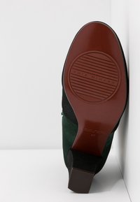 Semelle d’une chaussure à talon en daim vert avec une semelle en caoutchouc marron comportant la marque « Chie Mihara » et un talon bloc, taille 37 indiquée sur la semelle.