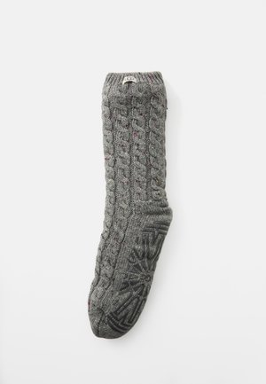 Gray knitted sock with a cable pattern, featuring multicolored flecks and a textured black rubber sole for grip. Label on cuff.