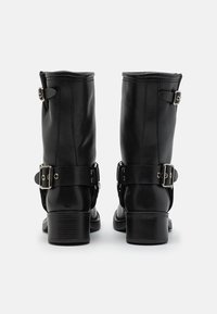 Botas de cuero negras hasta el tobillo con cremalleras traseras, correas ajustables y detalles de metal plateado. Punta cuadrada y tacones bajos apilados.