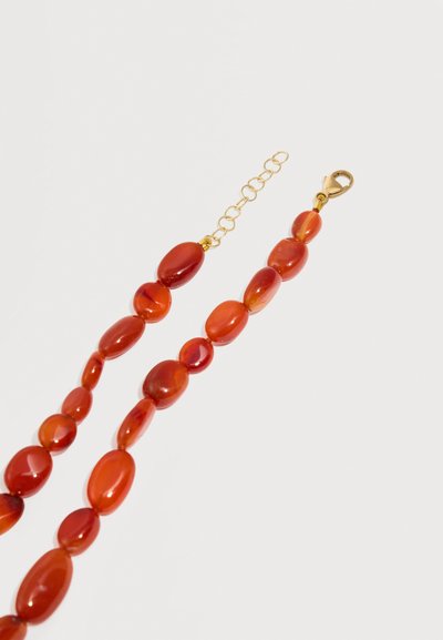 Brin de perles ovales rouge-orange poli avec fermoir mousqueton doré et chaîne réglable sur fond blanc.