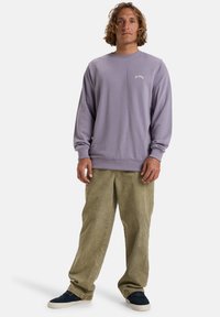 Lavendelfleece sweatshirt med ribbad krage, ihopparad med beiga kordbyxor. Skorna är mörkblå med vita sulor.