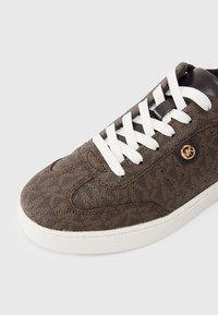 Καφέ αθλητικό παπούτσι με σχέδιο, λευκ ά κορδόνια, δερμάτινες λεπτομέρειες και στρογγυλεμένη μύτη. Διαθέτει λογότυπο και υφασμάτινο επάνω μέρος με υφή.