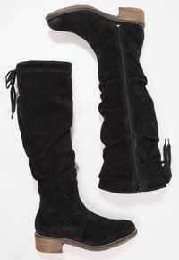 Botas de ante negras hasta la rodilla con un diseño holgado, cremallera lateral y un tacón marrón texturizado para mayor agarre.