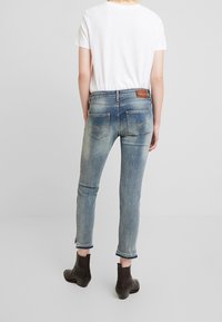 Jeans ajustados de color azul con un acabado descolorido, dos bolsillos traseros y una etiqueta de marca de cuero. Combinados con una camiseta blanca y botas negras hasta el tobillo.