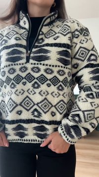 Γυναίκα που φοράει φλις πουλόβερ με ασπρόμαυρο μοτίβο και μισό φερμουάρ στον γιακά, όρθια με το ένα χέρι στην τσέπη της, σε εσωτερικό χώρο.