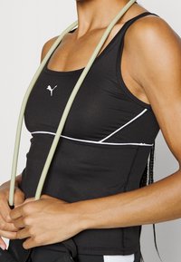 Canotta sportiva nera con cuciture bianche e un piccolo logo. Presenta spalline regolabili e un design aderente. Caratterizzata da una texture liscia.