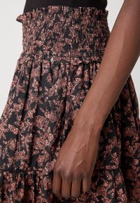 Bras à la peau foncée reposant à côté d'une jupe noire fleurie avec une taille froncée smockée et des détails volants.