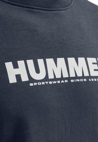 Marineblaue Sweatshirt mit weißem, fettem Text "HUMMEL" und kleinerem Text "SPORTSWEAR SINCE 1923" auf der Brust.