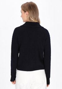 Maglione lavorato a maglia di colore blu navy con una finitura testurizzata, caratterizzato da un ampio colletto e polsini a coste. Il design prevede una vestibilità leggermente ampia.