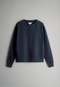 Marineblauw henley-shirt met lange mouwen, zeven knopen, geribbelde manchetten en een ronde halslijn op een effen grijze achtergrond.