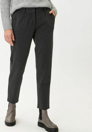 Persoon die donkergrijze op maat gemaakte broek, lichtgrijze trui en taupekleurige chunky enkellaarzen draagt, staand met één hand in de zak.