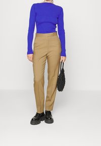 Dopasowany, długorękawowy fioletowy top o prążkowanej fakturze, zestawiony z dopasowanymi beżowymi spodniami. Całość uzupełnia czarna torebka i błyszczące czarne buty.