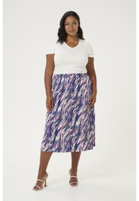 Jupe maxi en bleu marine avec un motif abstrait ondulé en rose et blanc, associée à un haut blanc à col en V à manches courtes. Sandales plates visibles.