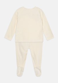 Grenouillère pour bébé couleur crème avec des manches longues, design pied-de-poule et texture douce. Tissu lisse, encolure ronde et manches à poignets.