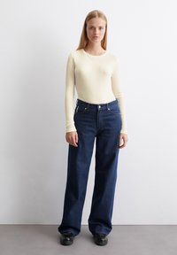 Ribbad, långärmad, krämfärgad topp kombinerad med högmidjade, vida, mörka jeans. Svarta skor fulländar outfiten.