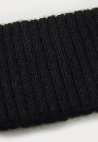 Nærbillede af blød sort ribstrik, der viser detaljeret tekstur og fibertråde på en hvid baggrund.