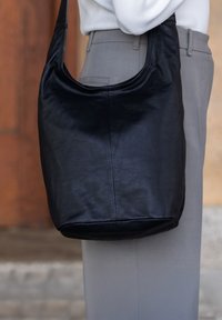 Black leather shoulder bag with a soft, smooth texture, curved top, and a rounded base, featured alongside light-colored pants.