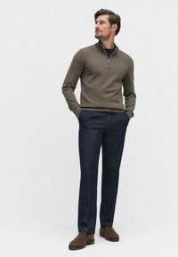 Brun, zip-up tröja med en texturerad yta; kombinerad med marinblå byxor och bruna mockascholor. Slim-fit design, modern skärning.