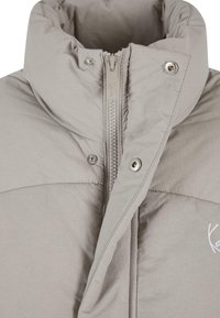 Chaqueta de plumas de color gris claro con un alto cuello, presenta un zipper central, botones de presión y detalles de costura sutiles. Textura suave.
