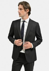 Svart kostym med satinfinish, ensidig design, tvåknappsstängning, utsvängda snibbar, matchad med vit skjorta och mörk slips.