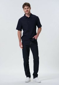 Chemise navy à manches courtes avec col, associée à un jean en denim foncé et des baskets blanches. Design simple et épuré avec des détails subtils.
