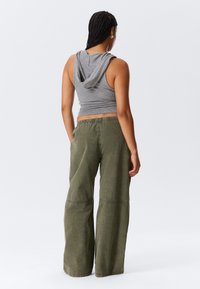 Gray sleeveless hoodie with a back flap, paired with loose-fitting olive green wide-leg pants featuring an elastic waistband and seam details.