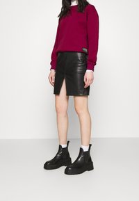 Sudadera burdeos, falda de cuero negra con abertura frontal y botas negras hasta el tobillo con suelas gruesas. Calcetines blancos visibles. Diseño simple.