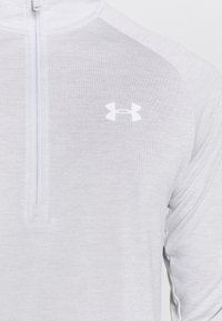 Vaaleanharmaa, pitkähihainen vetoketjullinen pusero, jossa teksturoitu kangas. Valkoinen Under Armour -logo ylävasemmalla puolella.