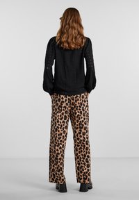 Černá texturovaná blůza s dlouhými nafouknutými rukávy, kombinovaná s béžovými kalhotami s leopardím potiskem a černými botami na podpatku.