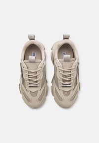 Beżowe sneakersy z panelami z siateczki, zaokrąglonymi gumowymi podeszwami i sznurowadłami; mają małą metkę z logo nad językiem i pętelkę z tyłu przy pięcie.