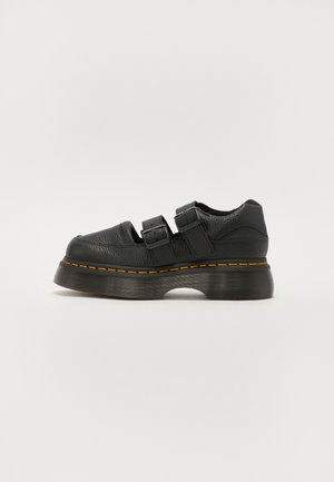 Zwarte leren schoen met twee verstelbare gespbandjes, verhoogde geprofileerde zool en zichtbare oranje stiksels langs de middenzool.