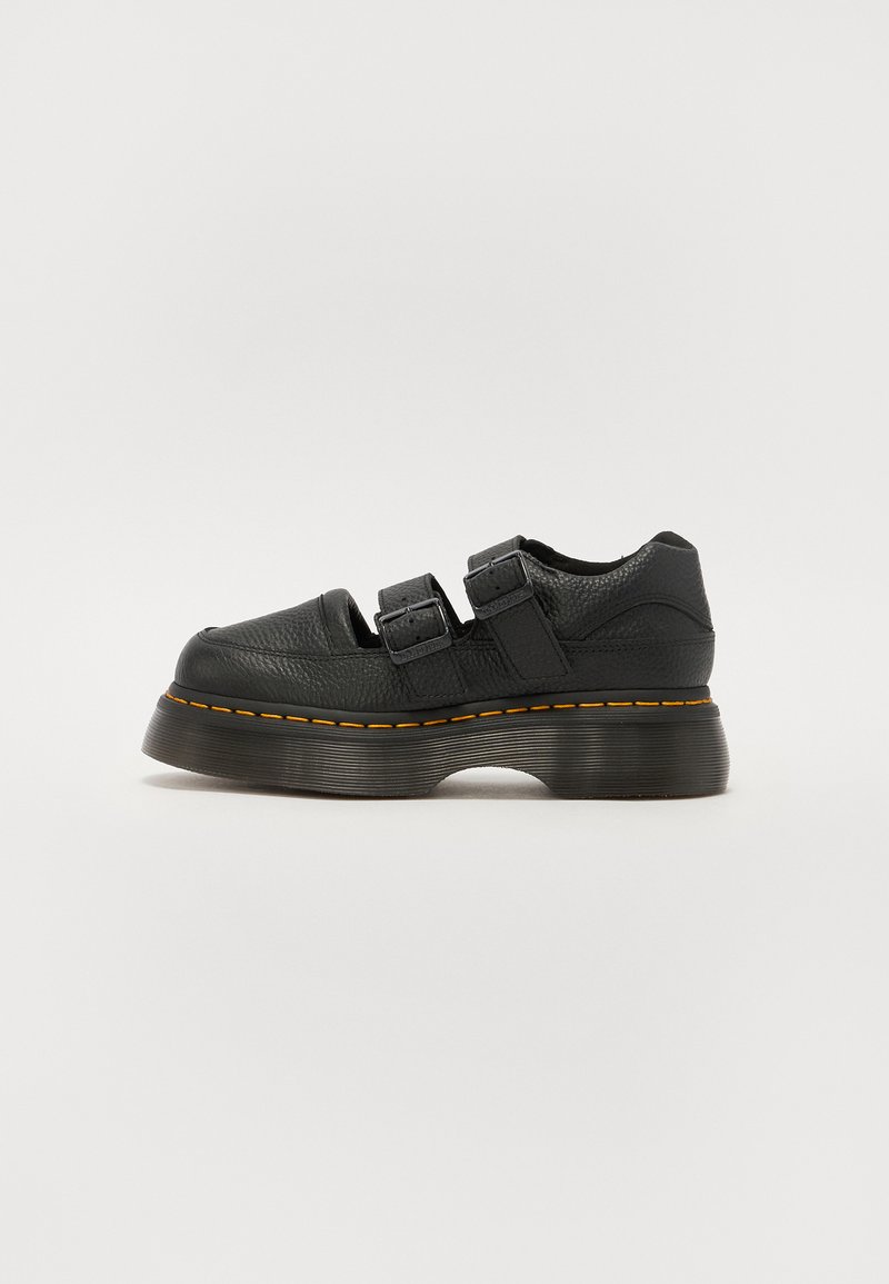 Black leather shoe with two adjustable buckle straps, raised textured sole, and visible orange stitching along the midsole.