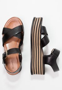 Black leather sandals with crisscross straps, a brown insole, and a striped platform sole. Features a buckle closure at the ankle.