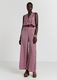 Top corto a righe rosa e nero con pantaloni larghi coordinati. Il tessuto appare leggero e testurizzato. Scarpe con piattaforma marroni.