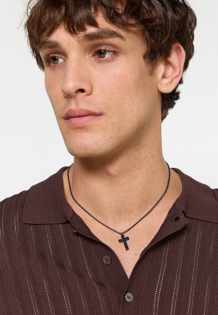 Collana con pendente a croce nera su una catena sottile, indossata sopra una camicia bordeaux con colletto, caratterizzata da strisce verticali e un tessuto testurizzato.