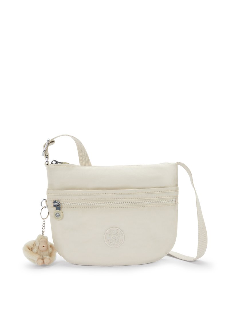 Beige crossover taske lavet af blødt stof med en lynlåslomme og logo. Den har en plysabe nøglering fastgjort til lynlåsen.