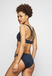 Navy blue bikini set featuring a strappy crop top with a cross-back design and matching high-waisted bottoms, both in smooth, stretchy fabric.