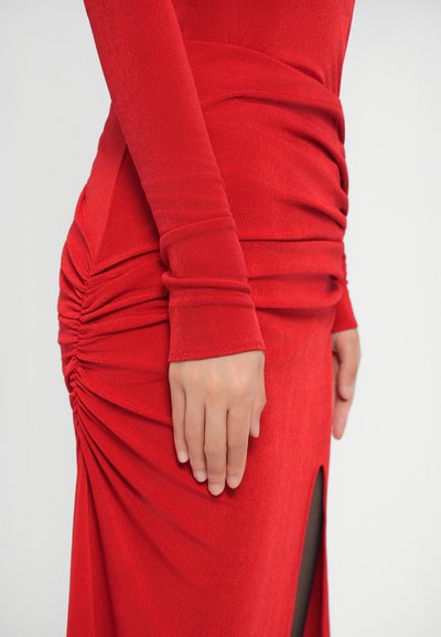Rode jurk met een aansluitende pasvorm, lange mouwen en geplooide textuur aan de zijkant. Inclusief een hoge split tot boven de dij voor extra detail.