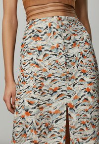 Falda larga en una tela ligera con un patrón abstracto en tonos naranja, negro y azul, abertura lateral y detalle de botones.