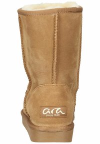 Beige Wildleder-Stiefelette mit abgerundeter Form, Fleece-Futter, gesteppten Details und einem Logopatch auf der Rückseite. Flache Gummisohle.