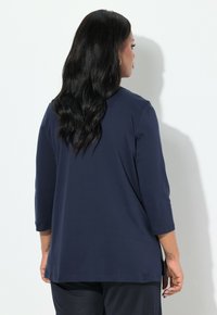 Marinblå tröja med långa ärmar, av avslappnad passform, rund halsringning och slitsar på sidorna. Slätt tyg med matt textur, utan mönster eller dekorationer.