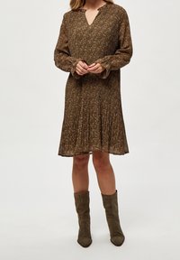 Ruskea kukallinen mekko, jossa on pitkät hihat, V-pääntie ja laskostettu hame. Yhdistetty oliivinvihreisiin kärkitossuihin. Silkkinen, teksturoitu kangas.