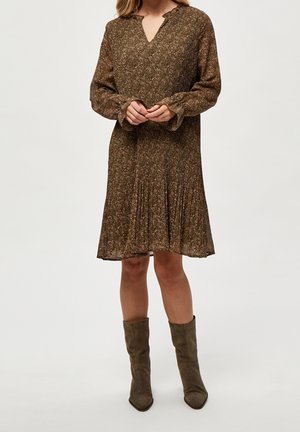 Robe florale marron avec des manches longues, décolleté en V et jupe plissée. Portée avec des bottes à bout pointu vert olive. Tissu lisse et texturé.